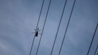 Ein Hubschrauber fliegt über Stromleitungen.