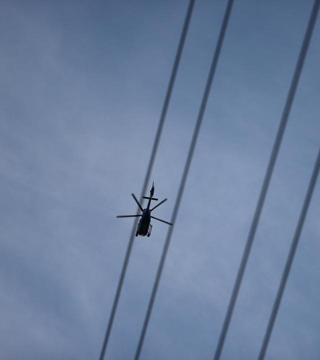 Ein Hubschrauber fliegt über Stromleitungen.