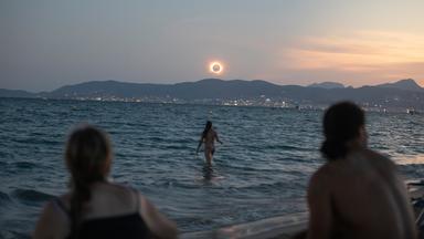 Eine Frau badet im Meer und weitere beobachten die totale Sonnenfinsternis am Strand von Palma.