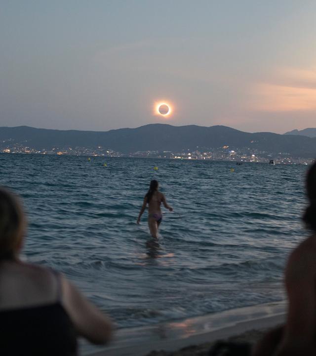 Eine Frau badet im Meer und weitere beobachten die totale Sonnenfinsternis am Strand von Palma.