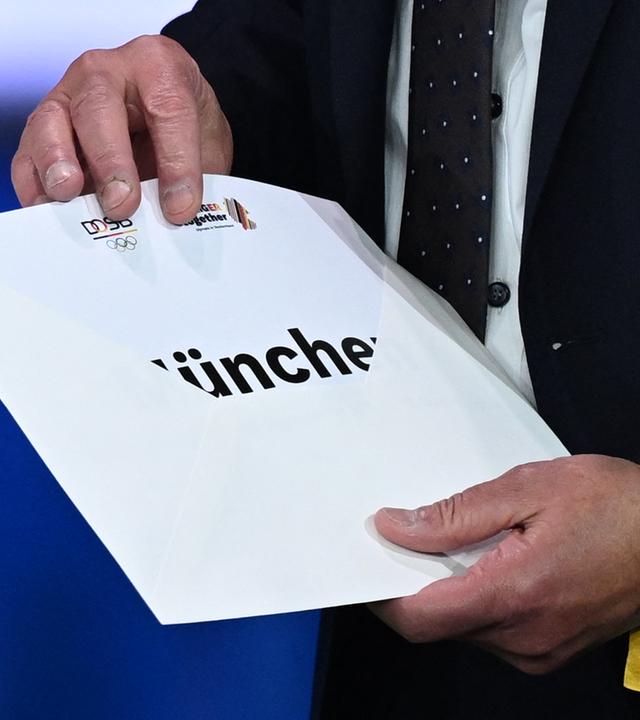 26.09.2026, Baden-Württemberg, Baden-Baden: Sportpolitik: Thomas Weikert, Präsident des Deutschen Olympischen Sportbundes (DOSB), öffnet auf der Bühne bei der außerordentlichen DOSB-Mitgliederversammlung zur Wahl des deutschen Olympia-Bewerbers für 2036, 2040 oder 2044 den Umschlag. München ist der deutsche Kandidat für Olympia und Paralympics für 2036, 2040 oder 2044.