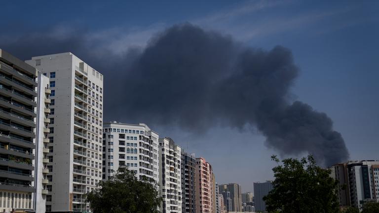 Vereinigte Arabische Emirate, Dubai: Ein Radfahrer fährt vorbei, als eine schwarze Rauchwolke aus einem Lagerhaus im Industriegebiet von Sharjah City in den Vereinigten Arabischen Emiraten aufsteigt, nachdem Berichte über iranische Angriffe eingegangen sind.