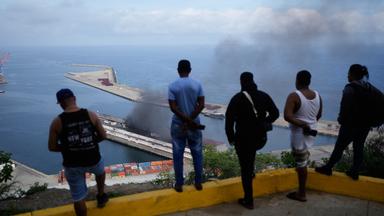 Männer beobachten, wie Rauch von einem Dock aufsteigt, nachdem im Hafen von La Guaira, Venezuela, am Samstag, 3. Januar 2026, Explosionen zu hören waren.