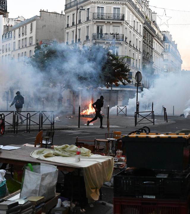 18.10.2026, Frankreich, Paris: Ein Demonstrant rennt durch Tränengas, während es auf einem Flohmarkt erneut Zusammenstöße zwischen Demonstranten und Polizeibeamten in Paris gibt