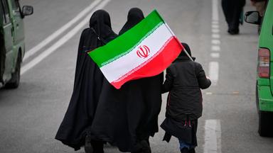 20.03.2026, Iran, Teheran: Zwei Frauen und ein Kind, die eine iranische Flagge halten, gehen zum Freitagsgebet zur Großen Moschee Imam Khomeini in der iranischen Hauptstadt.