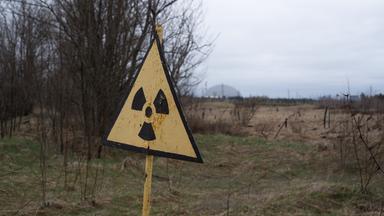 09.04.2026, Ukraine, Tschernobyl: Ein Radioaktivitäts-Warnzeichen, im Hintergrund das Kernkraftwerk Tschernobyl, aufgenommen am 9. April 2026. Was als harmloser Sicherheitstest begann, entwickelte sich am 26. April 1986 zur bedeutendsten Atomkatastrophe der Geschichte. An diesem Tag explodierte Reaktor 4 des Wladimir-Iljitsch-Lenin-Kernkraftwerks, weitläufig bekannt als Kernkraftwerk Tschernobyl
