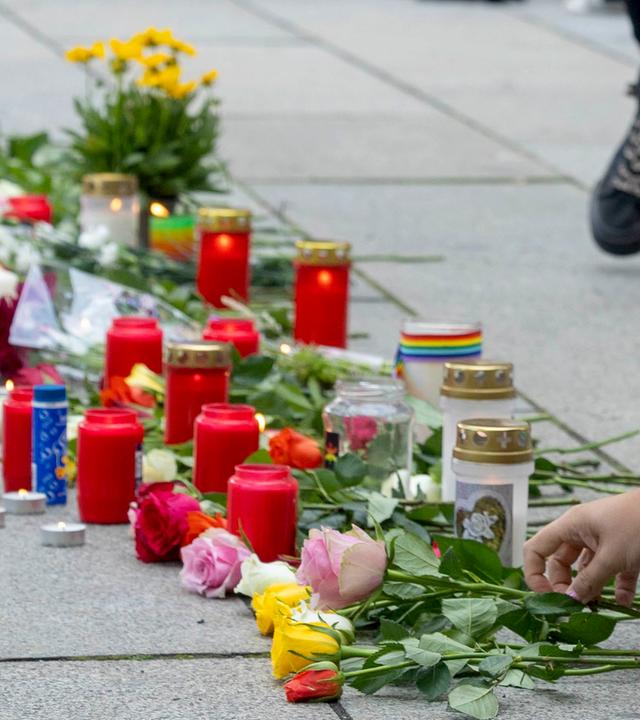 Ein Frau legt Blumen nieder. Auch Kerzen werden bei der Mahnwache zum Anschlag auf den CSD in Berlin von Queer Pride Dresden und weiterer Gruppen auf den Boden vor einer Regenbogenfahne gestellt.