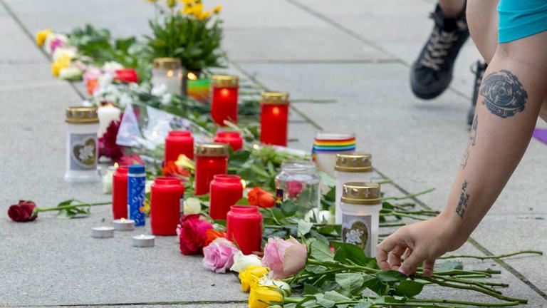 Ein Frau legt Blumen nieder. Auch Kerzen werden bei der Mahnwache zum Anschlag auf den CSD in Berlin von Queer Pride Dresden und weiterer Gruppen auf den Boden vor einer Regenbogenfahne gestellt.