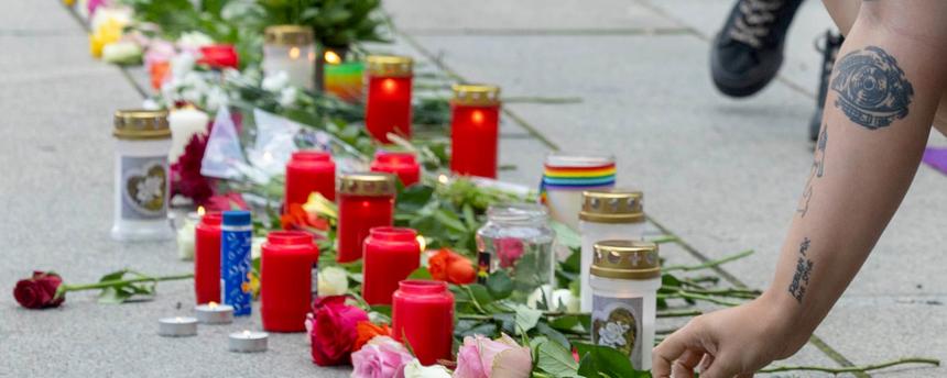 Ein Frau legt Blumen nieder. Auch Kerzen werden bei der Mahnwache zum Anschlag auf den CSD in Berlin von Queer Pride Dresden und weiterer Gruppen auf den Boden vor einer Regenbogenfahne gestellt.