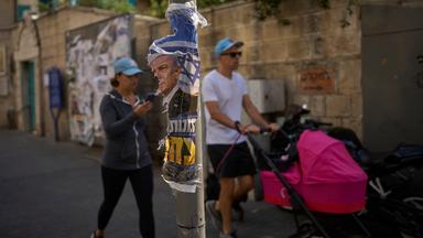 28.10.2026, Israel, Jerusalem: Ein Mann und eine Frau gehen einen Tag nach den Wahlen an einem zerrissenen Wahlplakat mit dem israelischen Ministerpräsidenten Benjamin Netanjahu vorbei. 