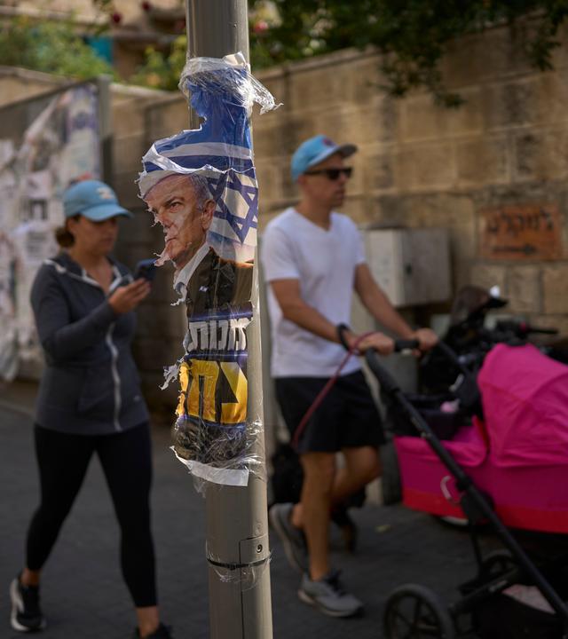 28.10.2026, Israel, Jerusalem: Ein Mann und eine Frau gehen einen Tag nach den Wahlen an einem zerrissenen Wahlplakat mit dem israelischen Ministerpräsidenten Benjamin Netanjahu vorbei. 