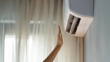 Der Wohnungseigentümer schaltet die Klimaanlage ein, überprüft das Bedienelement und streckt die Hand in den Luftstrom.