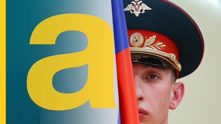 Ein russischer Soldat mit Soldatenhut. Sein Gesicht wird zur Hälfte von einer russischen Flagge verdeckt.