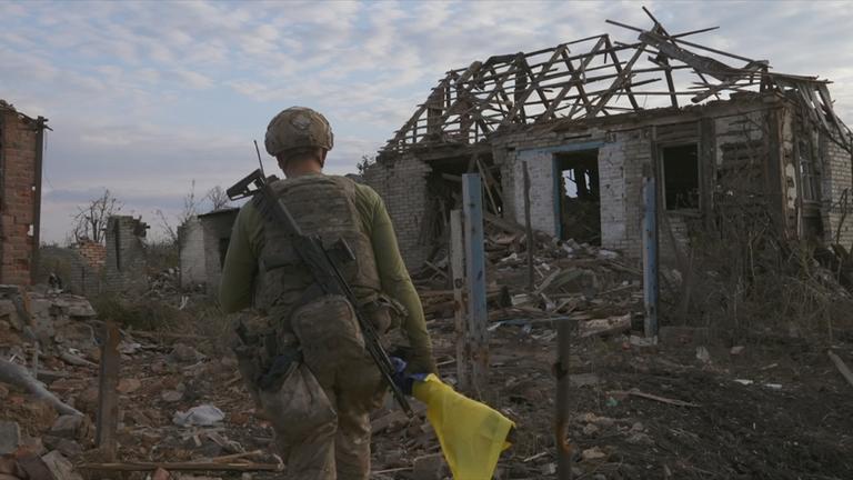 Ukrainischer Soldat läuft auf zerstörtes Haus zu.