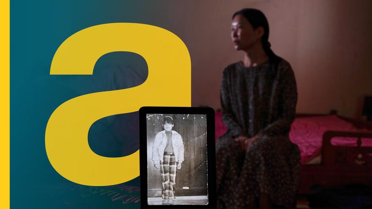 Eine Frau sitzt in einem abgedunkelten Raum, vorne steht ein Tablet und zeigt ein historisches Foto von ihr als Kind.