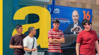 Wahlplakat des armenischen Präsidenten, davor stehen Jugendliche.