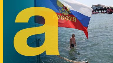 Mann badet im Schwarzen Meer in Sotschi, neben ihm eine Russland-Fahne.