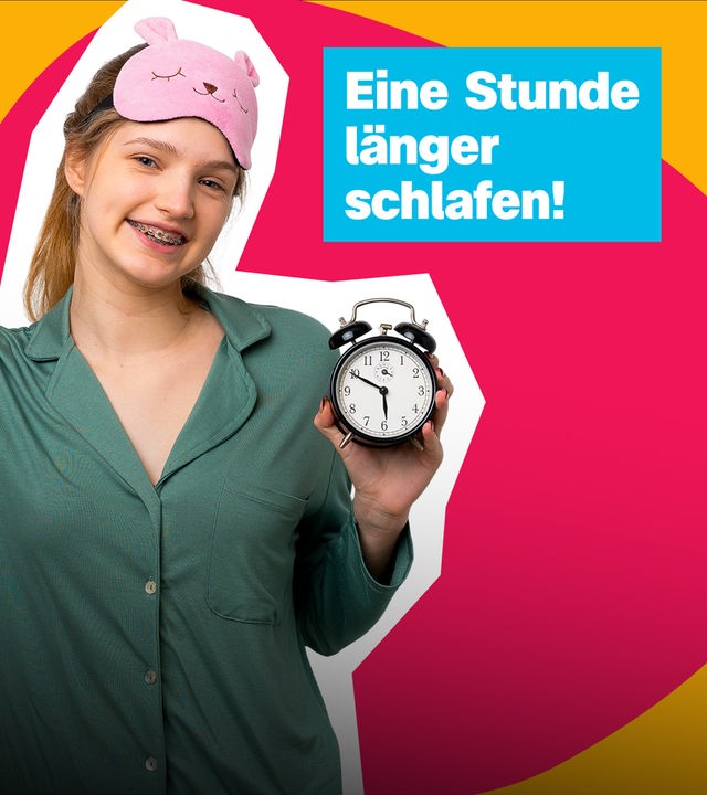 Eine Stunde länger schlafen!; Ein Mädchen mit rosa Schlafmaske auf dem Kopf hält jubelnd einen Wecker hoch.