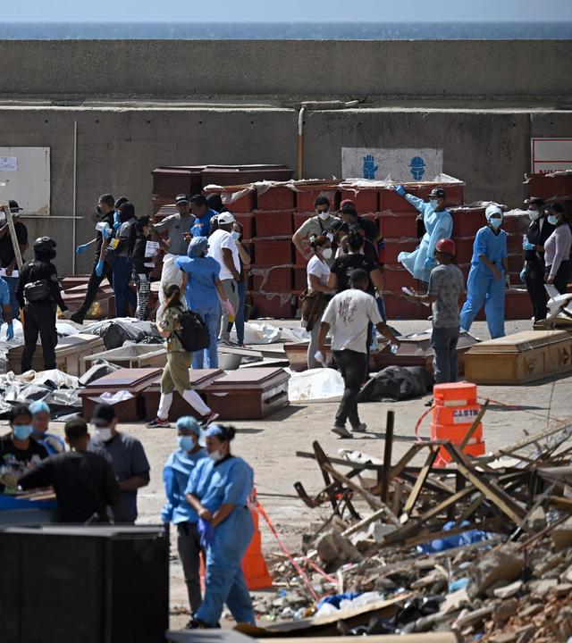 Graphic content / Forensic experts carry out body identification work on corpses laid out on the ground near coffins at a makeshift morgue in the port of La Guaira, La Guaira State, Venezuela on June 29, 2026, following the June 24 twin earthquakes. Hopes were fading on June 29, 2026 of finding survivors more than four days after powerful twin earthquakes struck Venezuela, as residents grow increasingly frustrated with the government's response to the disaster that has killed at least 1,450 people and left tens of thousands unaccounted for.