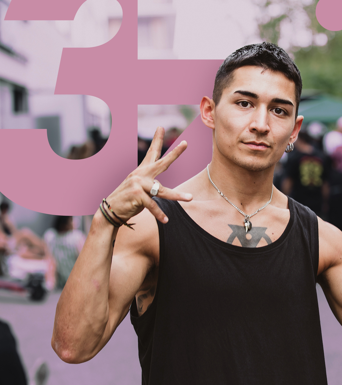 Ein junger Mann posiert auf der Straße, im Hintergrund, verschwommen zu erkennen, stehen einige Menschen beisammen