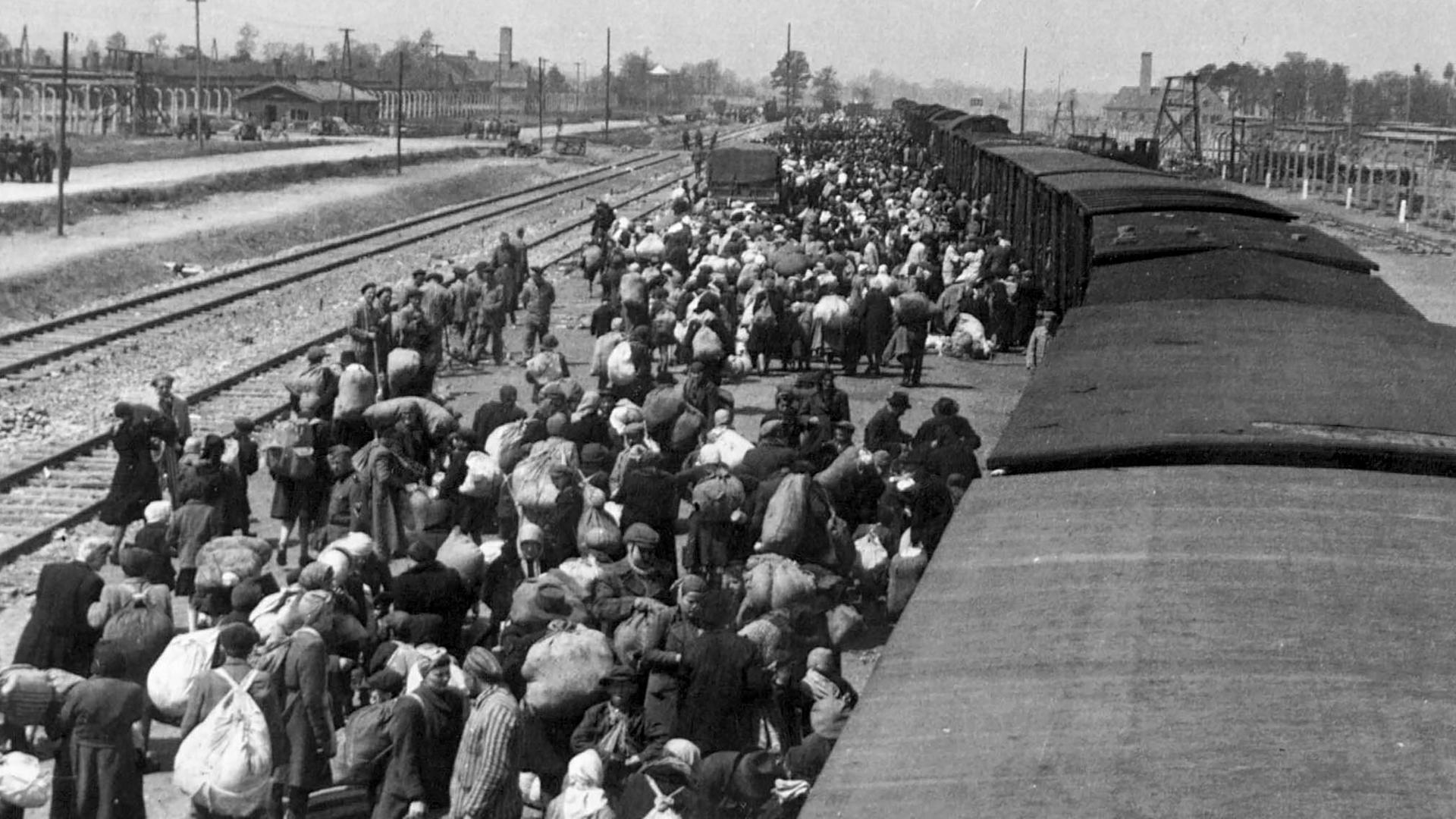 KZ Auschwitz-Birkenau - Bernhard Walter geht fotografierend über die Waggondächer in Richtung Zugmitte. Die Menschen noch mit ihrem Gepäck in die gleiche Richtung. 