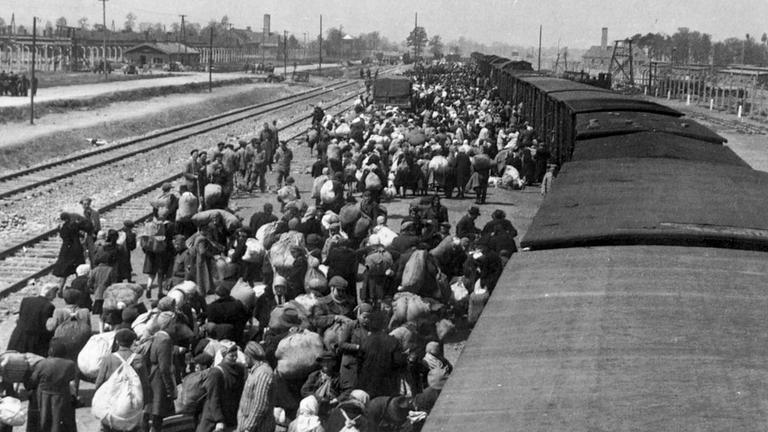 KZ Auschwitz-Birkenau - Bernhard Walter geht fotografierend über die Waggondächer in Richtung Zugmitte. Die Menschen noch mit ihrem Gepäck in die gleiche Richtung. 