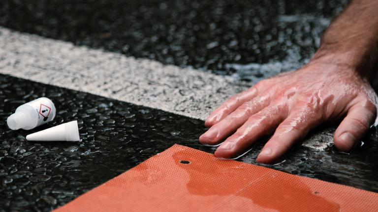 Die Hand eines Aktivisten der Letzten Generation ist auf der Straße festgeklebt.