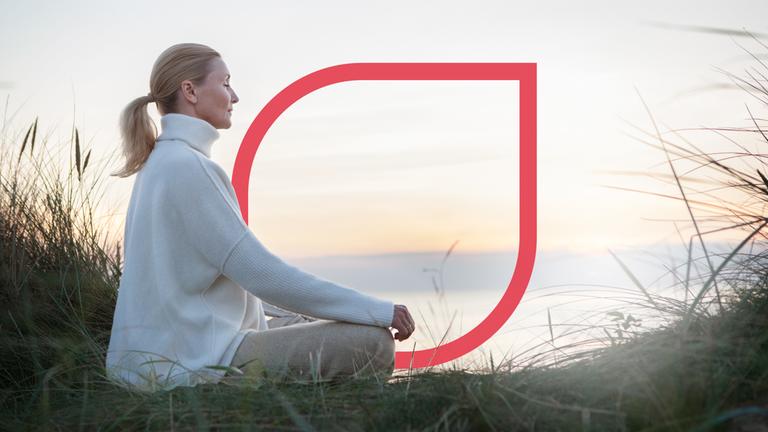 Eine Frau meditiert bei Sonnenuntergang am Meer