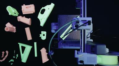 3D-gedruckte Waffenteile liegen neben einem 3D-Drucker.