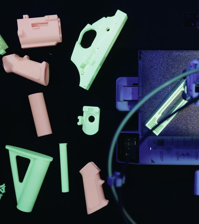 3D-gedruckte Waffenteile liegen neben einem 3D-Drucker.