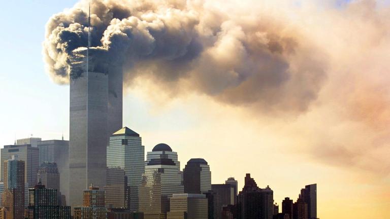 Panorama von Manhattan am 11. September 2001 mit Fokus auf das World Trade Center, dessen oberer Bereich von einer massiven Rauchwolke umhüllt ist.