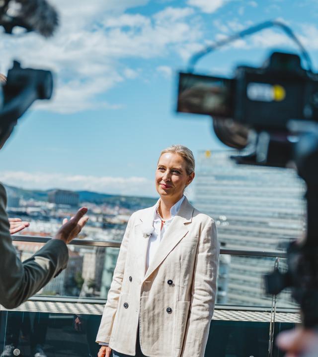Alice Weidel "Berlin direkt - Sommerinterview 2026": Alice Weidel steht auf einer Terrasse, TV Kameras stehen vor ihr.