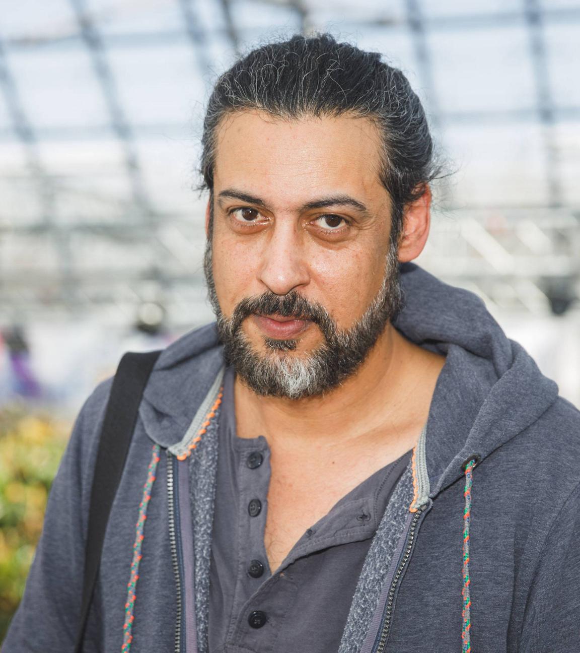 Porträtfoto eines Mannes mit zurückgebundenen graumelierten Haaren und Bart.