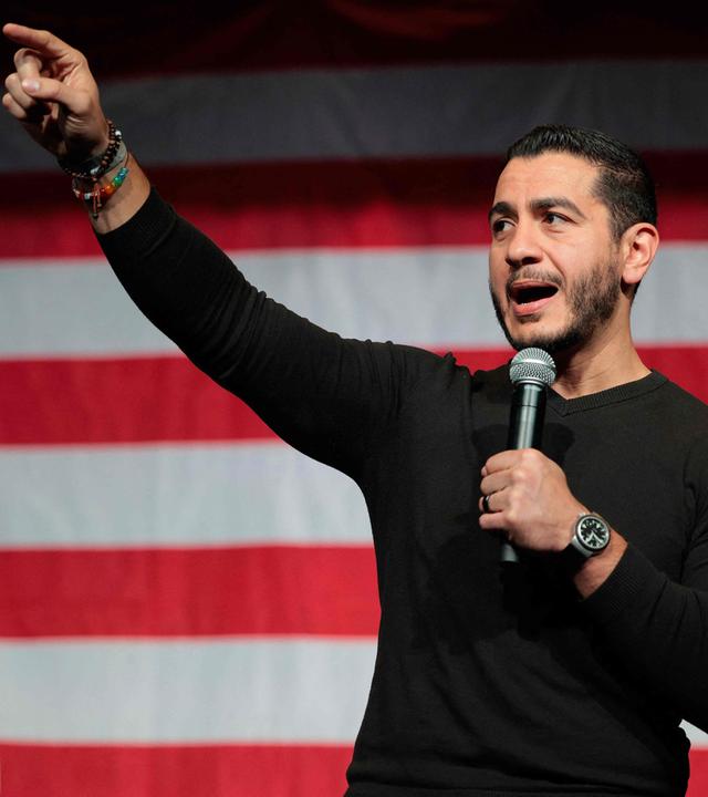 Der demokratische Kandidat Abdul El-Sayed bei einem Auftritt in Michigan vor einer großen USA-Flagge. Er gestikuliert ins Publikum.