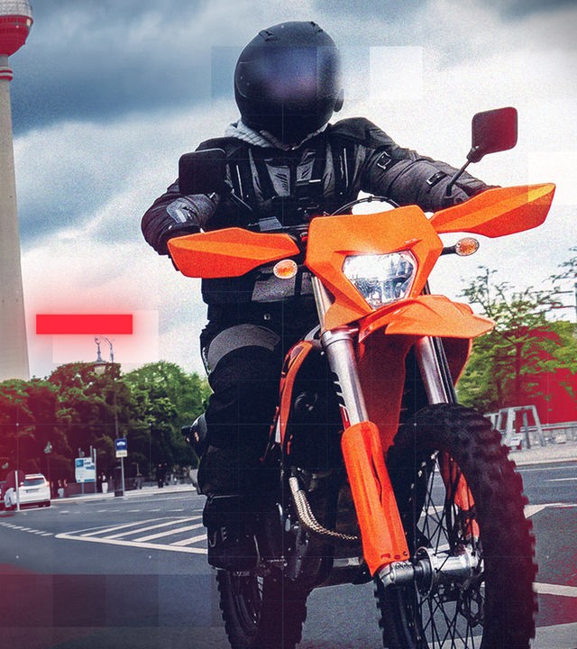 Motorradfahrer in schwarzer Schutzkleidung und mit dunklem Helm fährt auf einem orangefarbenen Enduro-Motorrad durch eine urbane Straßenszene. Im Hintergrund sind weitere Fahrzeuge, moderne Gebäude und der Berliner Fernsehturm zu sehen. Dunkle Wolken am Himmel sowie rote und transparente grafische Overlay-Elemente mit Rasterstruktur verleihen dem Motiv einen dynamischen, technologischen und aufmerksamkeitsstarken Charakter.