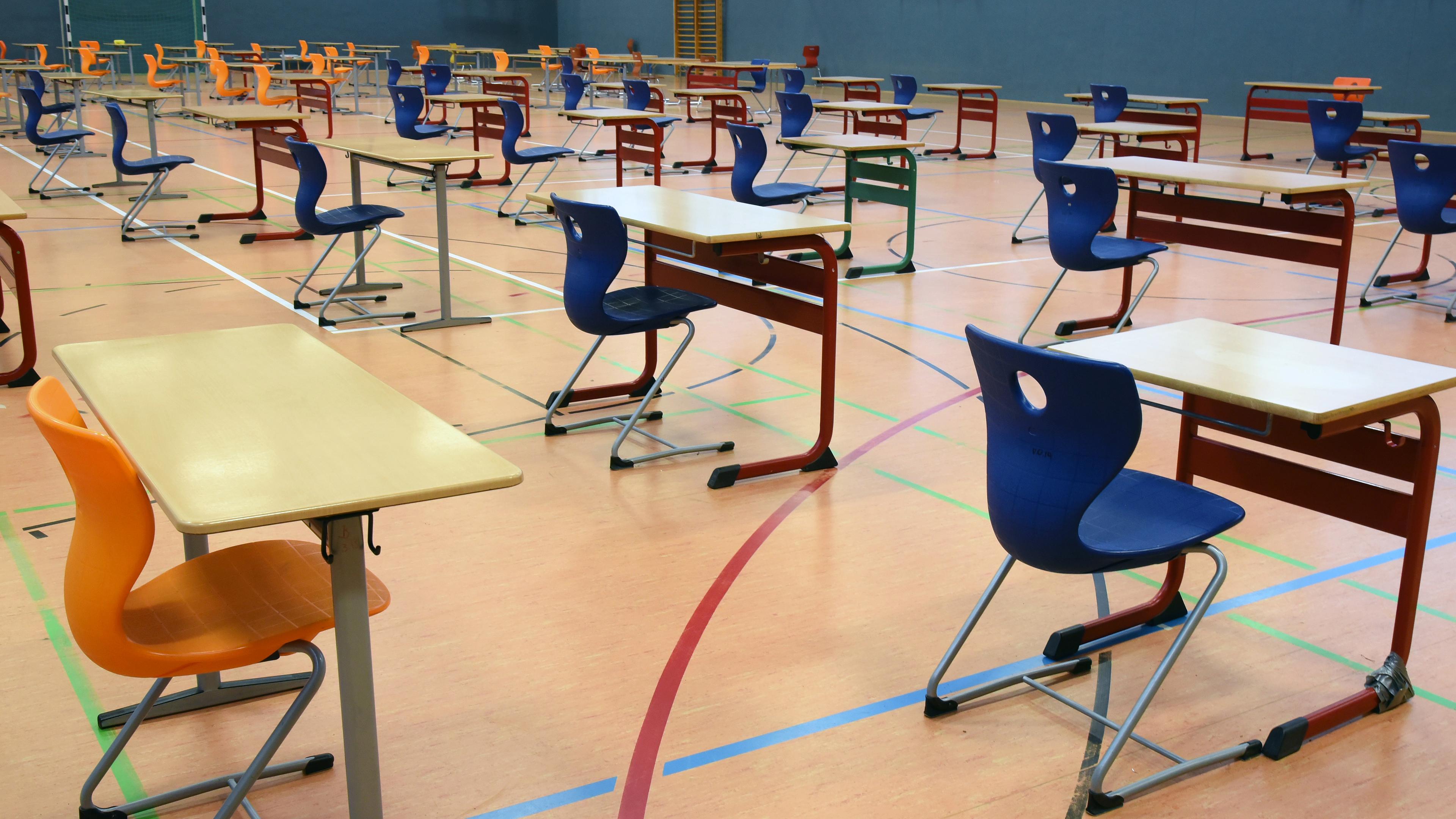 Mit großen Abständen stehen Tische und Stühle in einer Turnhalle in Leipzig