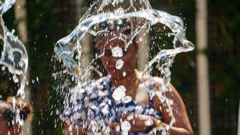 Eine Frau steht vor einer Wasserfontäne in einer Stadt