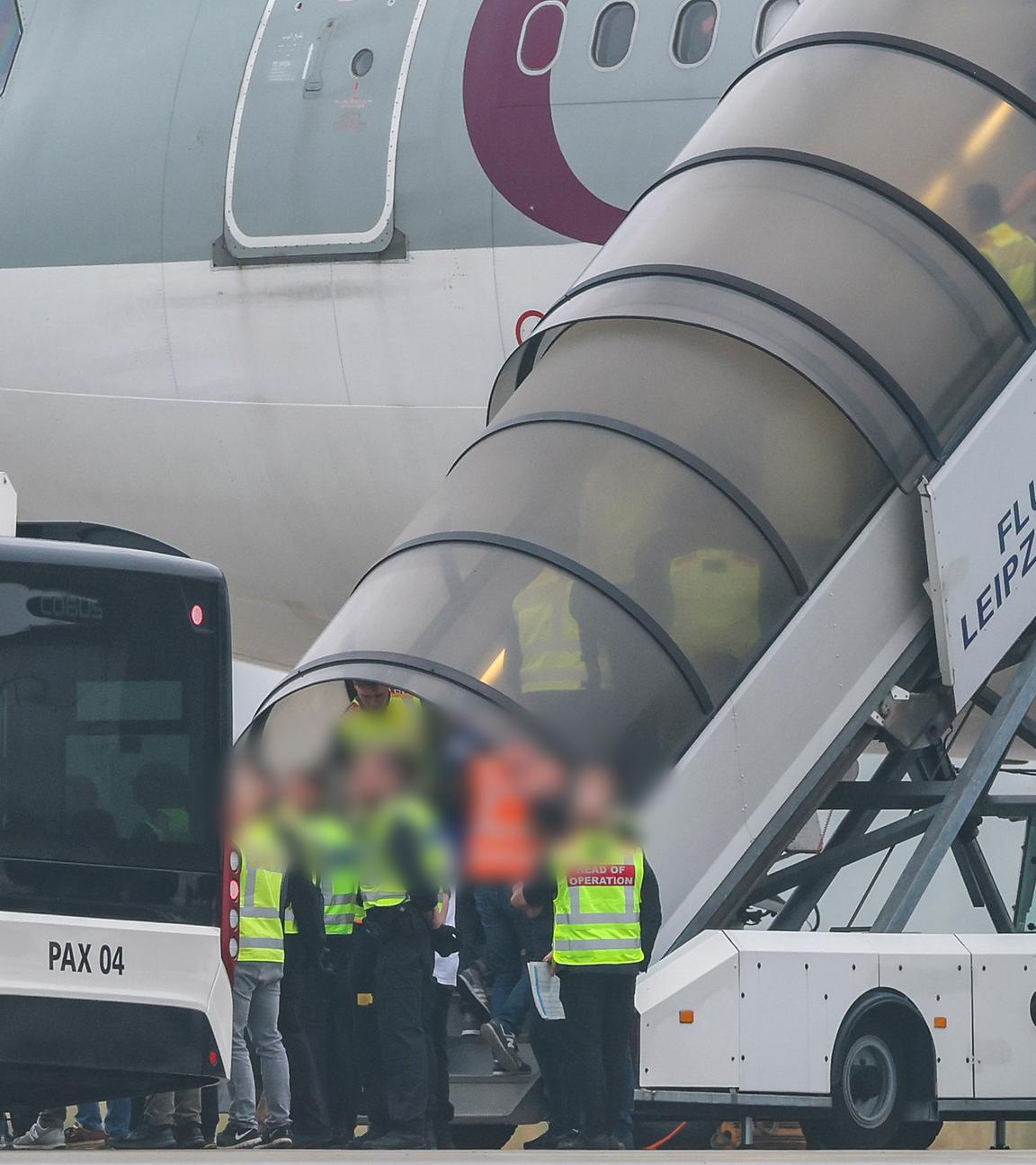 Menschen besteigen ein Flugzeug der Qatar Airways, vor dem Beamte der Bundespolizei stehen, auf dem Vorfeld am Flughafen Leipzig/Halle.