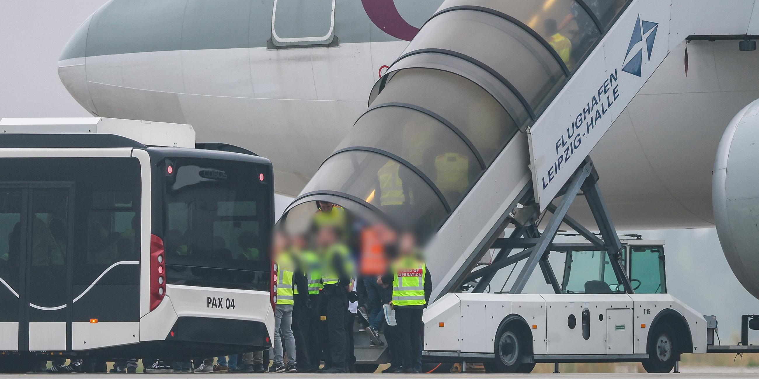 Menschen besteigen ein Flugzeug der Qatar Airways, vor dem Beamte der Bundespolizei stehen, auf dem Vorfeld am Flughafen Leipzig/Halle.