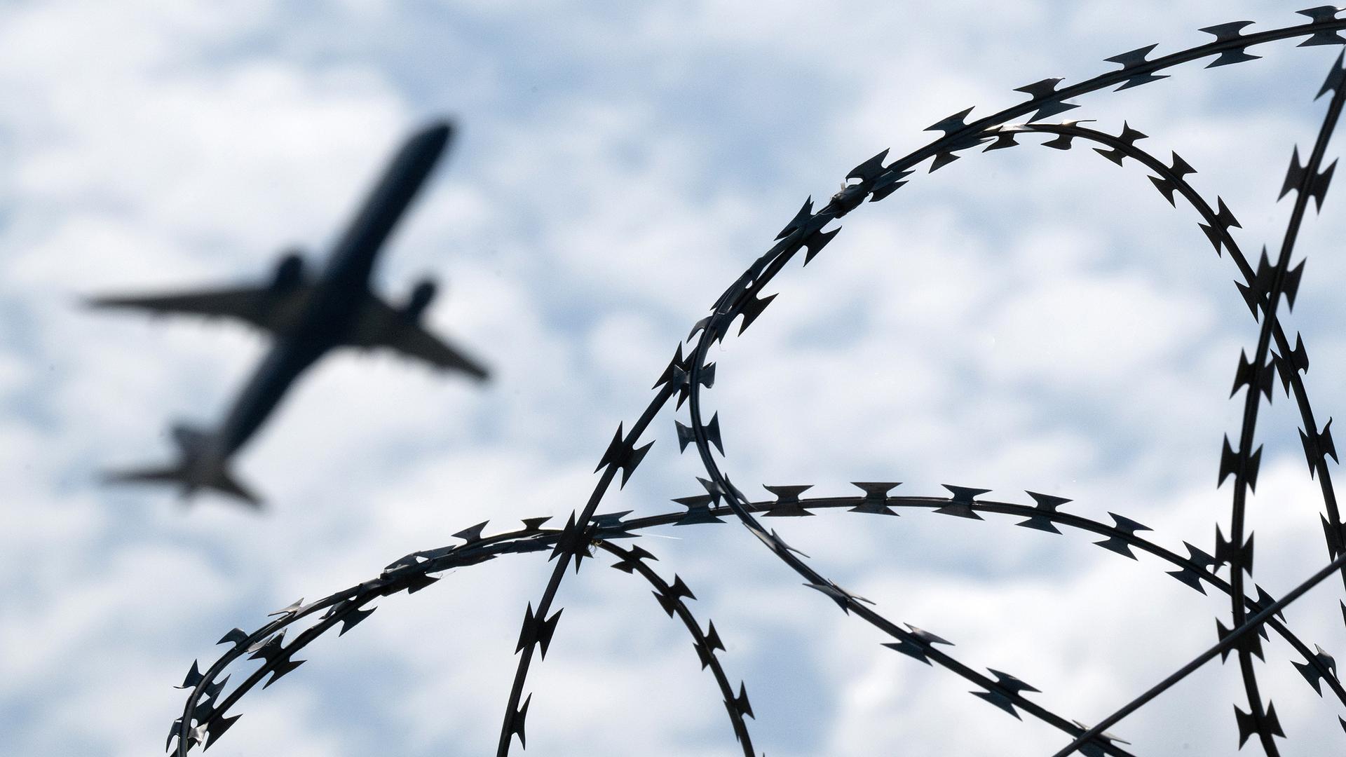 Ein Flugzeug hebt am Flughafen BER hinter einem Zaun mit Natodraht ab