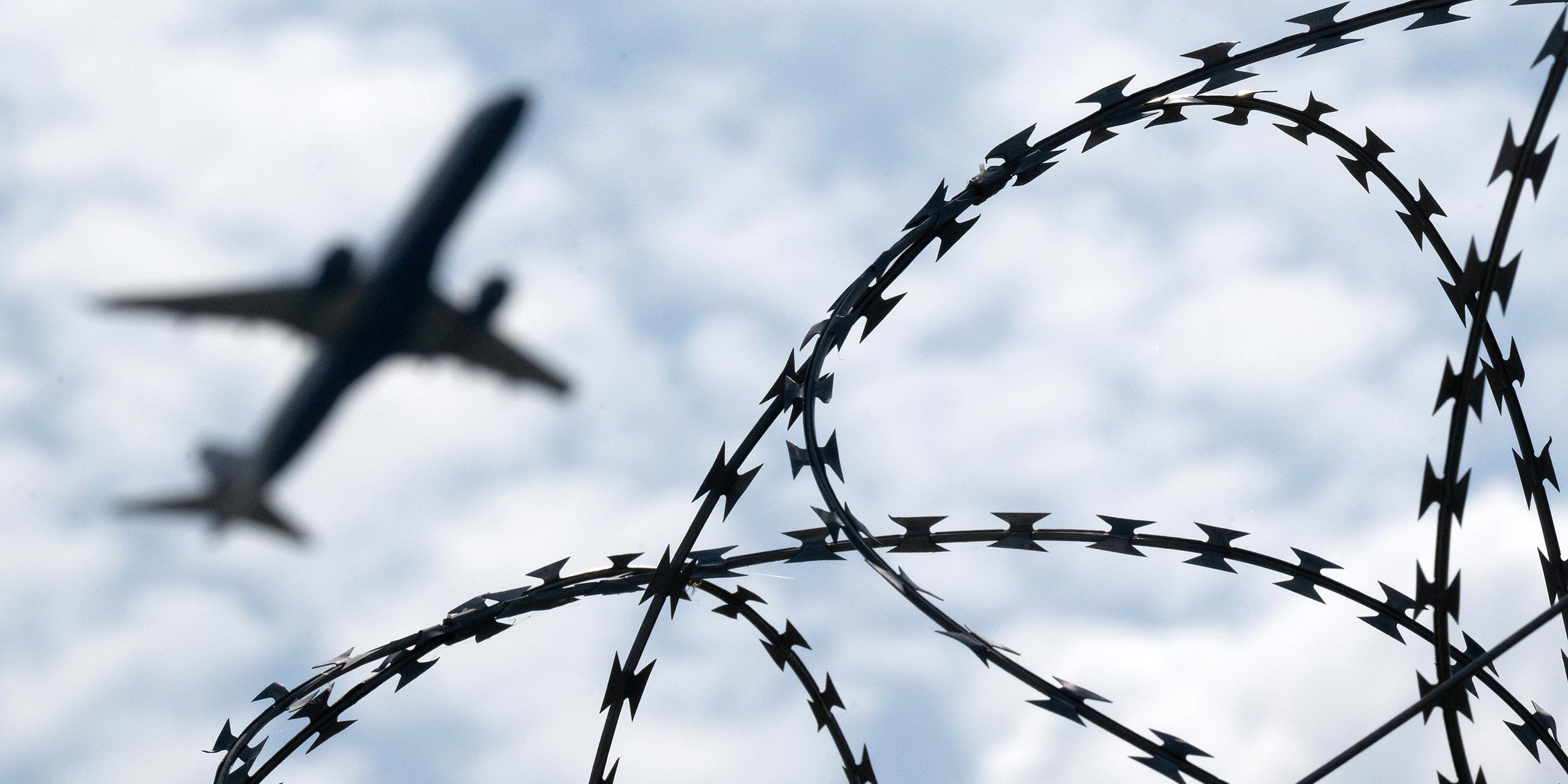 Ein Flugzeug hebt am Flughafen BER hinter einem Zaun mit Natodraht ab