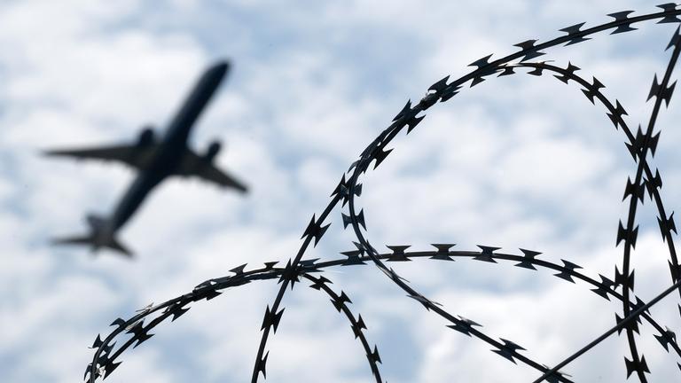 Ein Flugzeug hebt am Flughafen BER hinter einem Zaun mit Natodraht ab