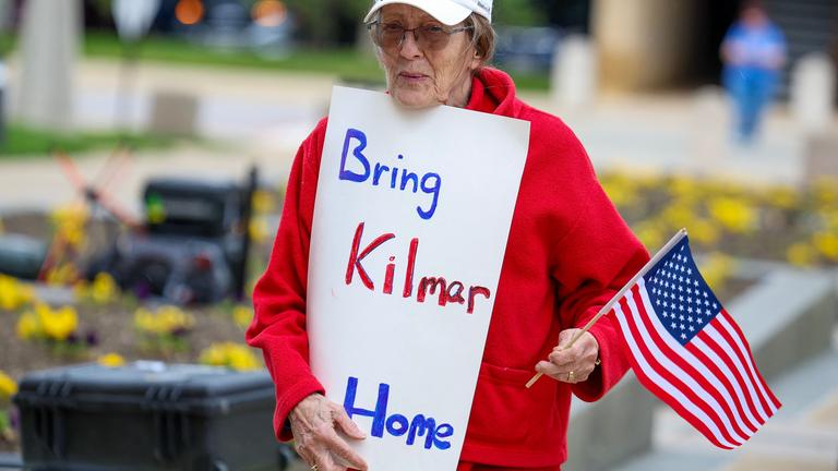 Eine Frau trägt auf einem Protest eine kleine US-Flagge und ein Schild mit der Aufschrift "Bring Kilmar Home".