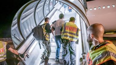 Polizeibeamte begleiten einen Afghanen auf dem Flughafen in ein Charterflugzeug