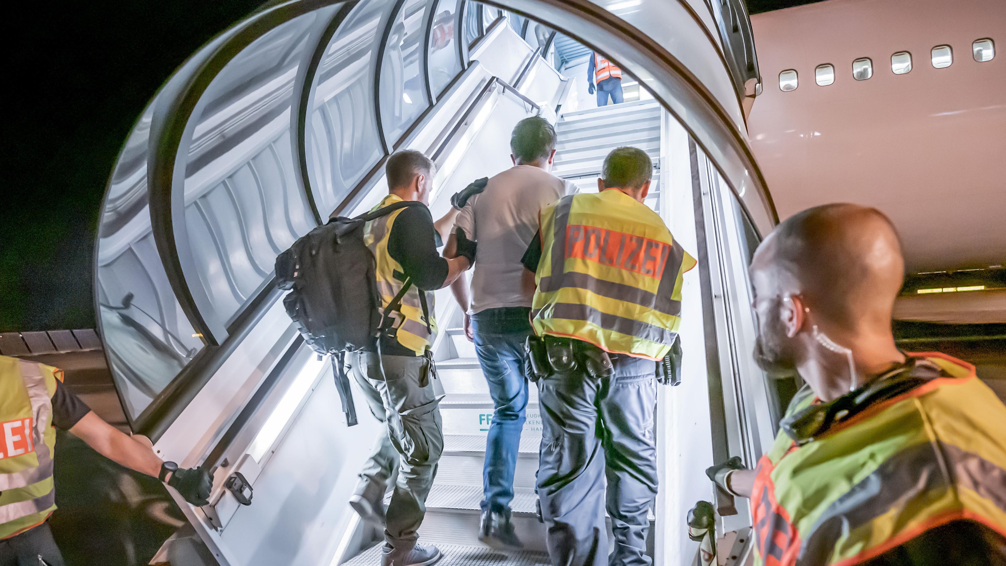 Ein Flüchtling wird von Polizisten in ein Flugzeug begleitet. 