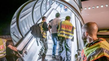 Ein Flüchtling wird von Polizisten in ein Flugzeug begleitet. 
