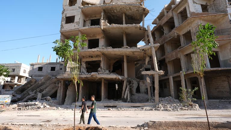 Auf dem Bild ist eine Ruine in Syrien zu sehen. Zwei Kinder laufen daran vorbei.