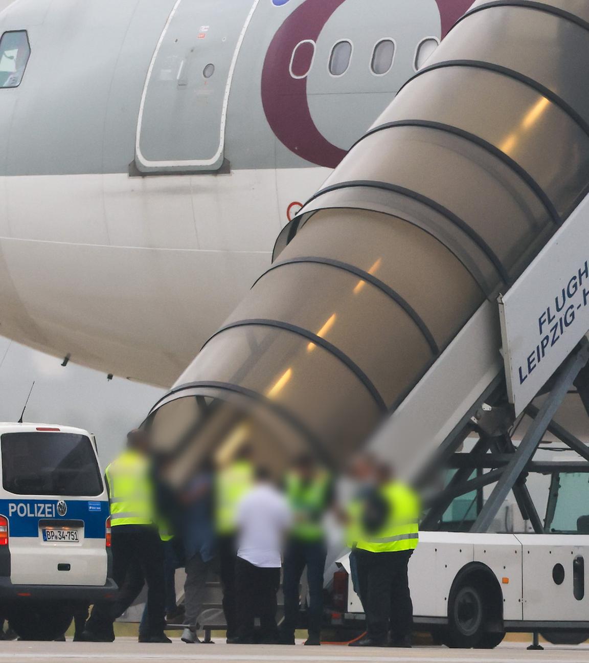 Menschen besteigen ein Flugzeug der Qatar Airways, vor dem Fahrzeuge der Bundespolizei stehen auf dem Vorfeld am Flughafen Leipzig/Halle.