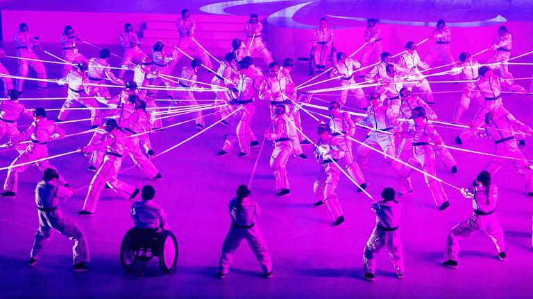 Künstler performen während der Abschlussfeier der Paralympics unter rosafarbenem Licht.