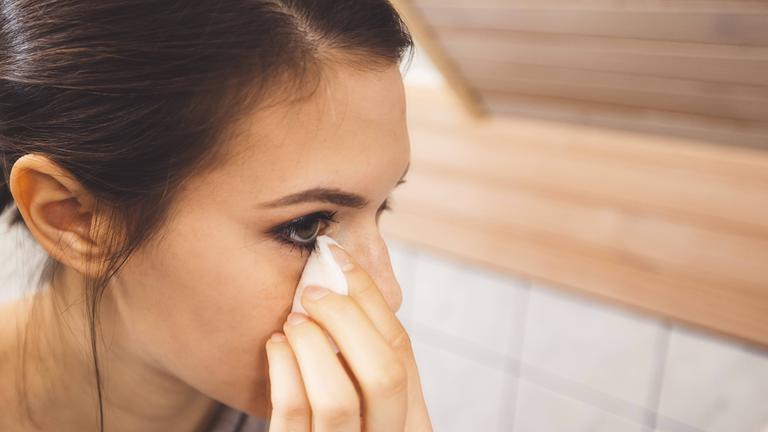 Junge Frau, die ihr Gesicht reinigt und Make up mit einem Wattepad und Mizellenwasser entfernt.